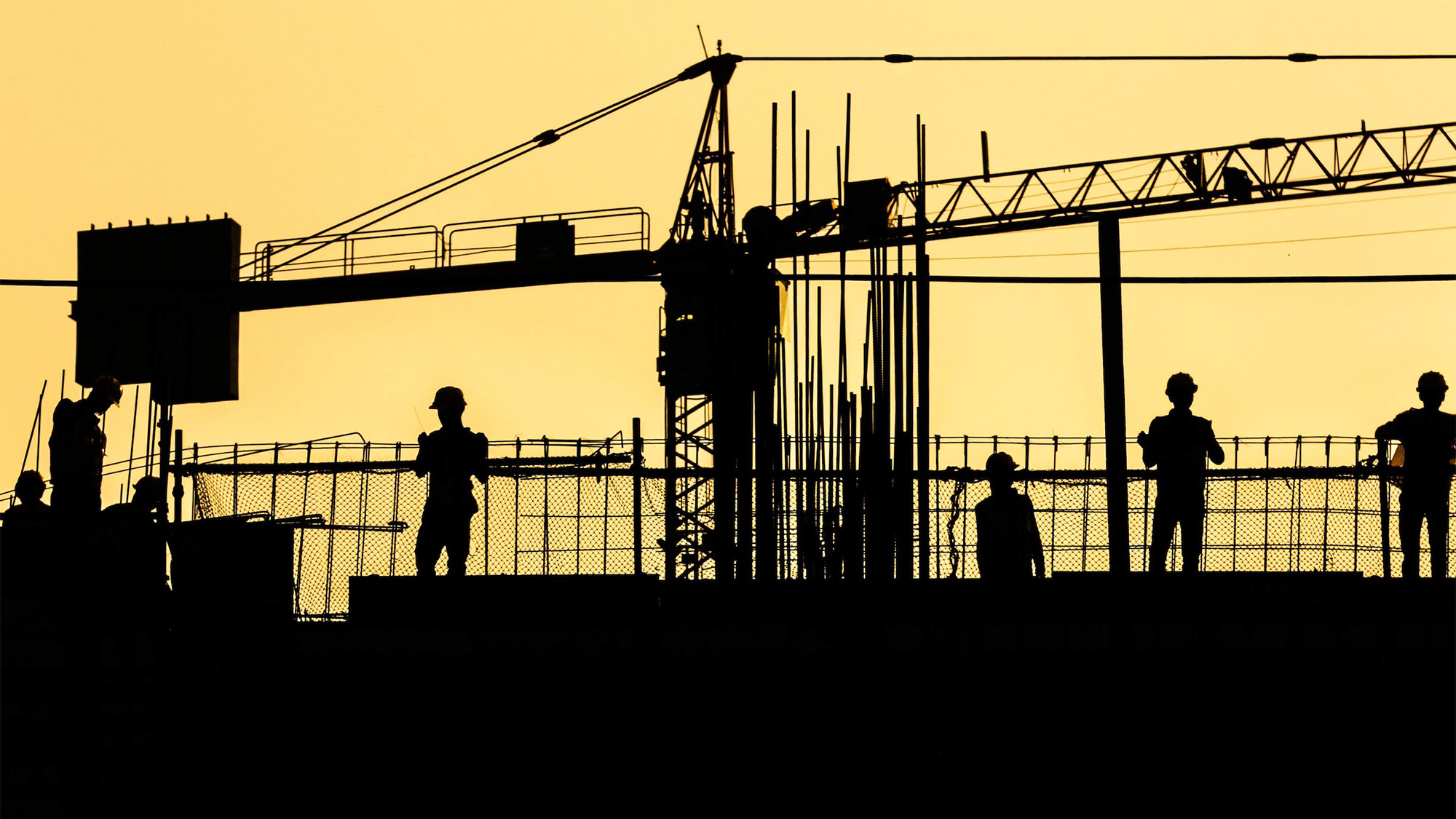 Construction works and a crane are silhouetted against a bright yellow sky