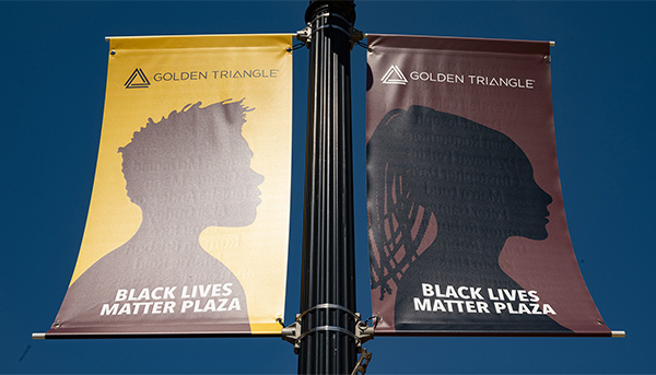Two banners depicting Black Lives Matter themes hang from a post