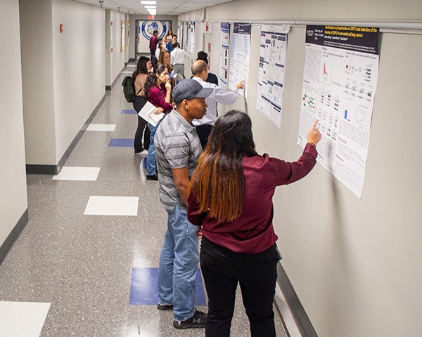 Students and onlookers stand in a hallway lined with scientific posters