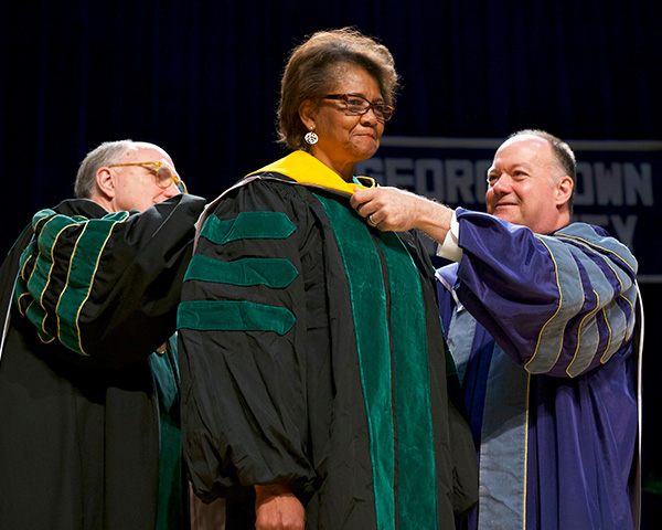 Dr. Mitchell and President DeGioia place the hood on McCaskill-Stevens' academic regalia