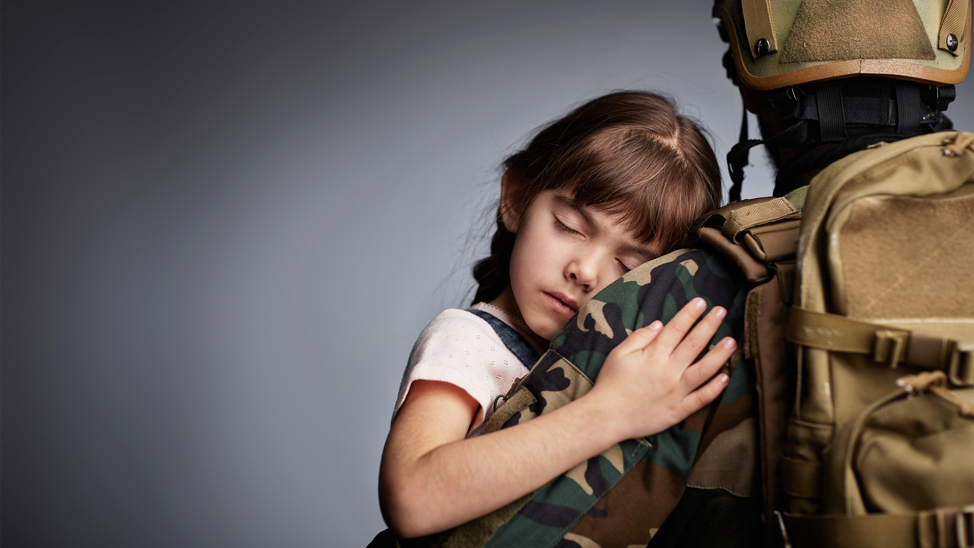 A young girls hugs a person in military fatigues
