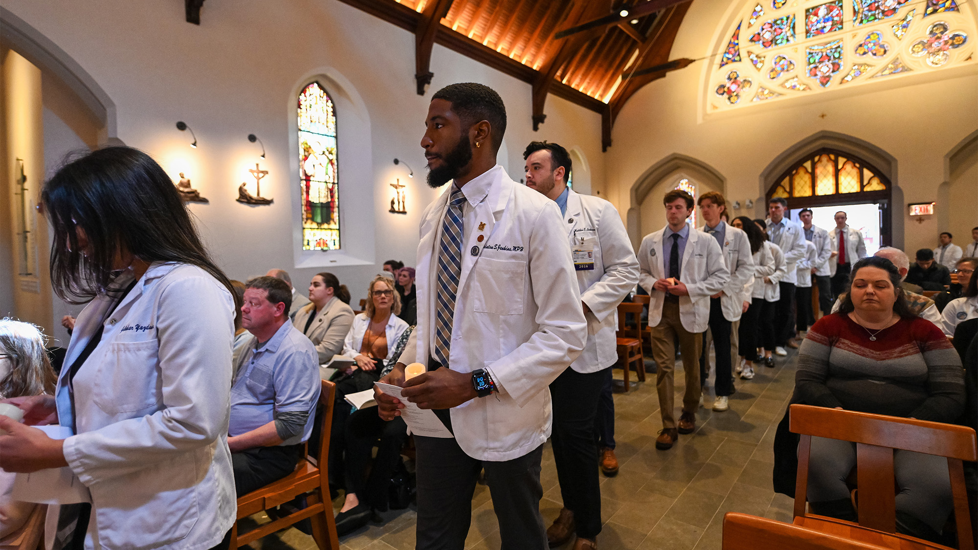 Medical students in white coats process into Dahlgren Chapel in a line