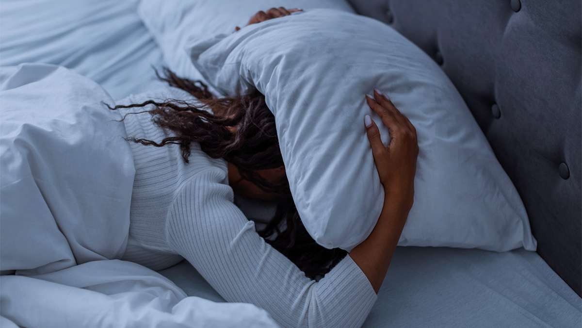 A women lies in bed with a pillow over her head