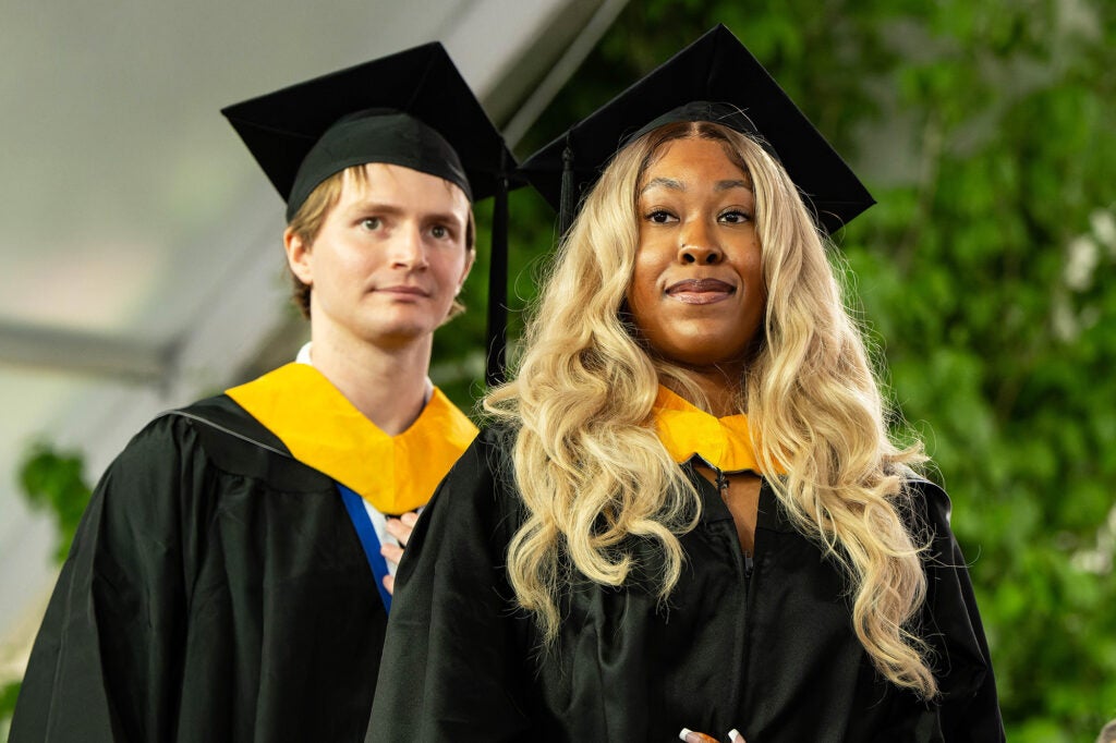 Two students stand side by side in academic regalia
