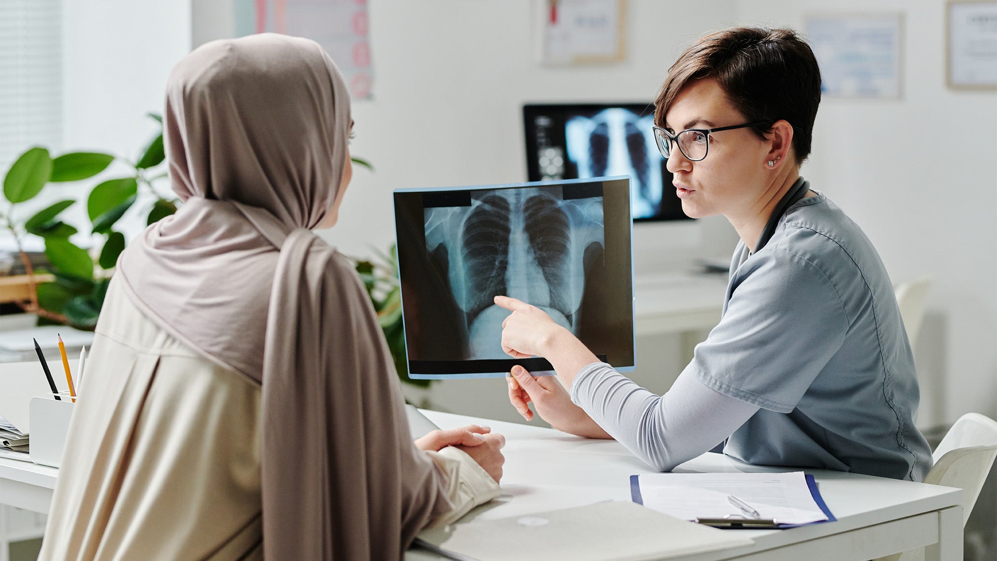 A health care provider points an xray result and speaks with a Muslim woman wearing a hijab