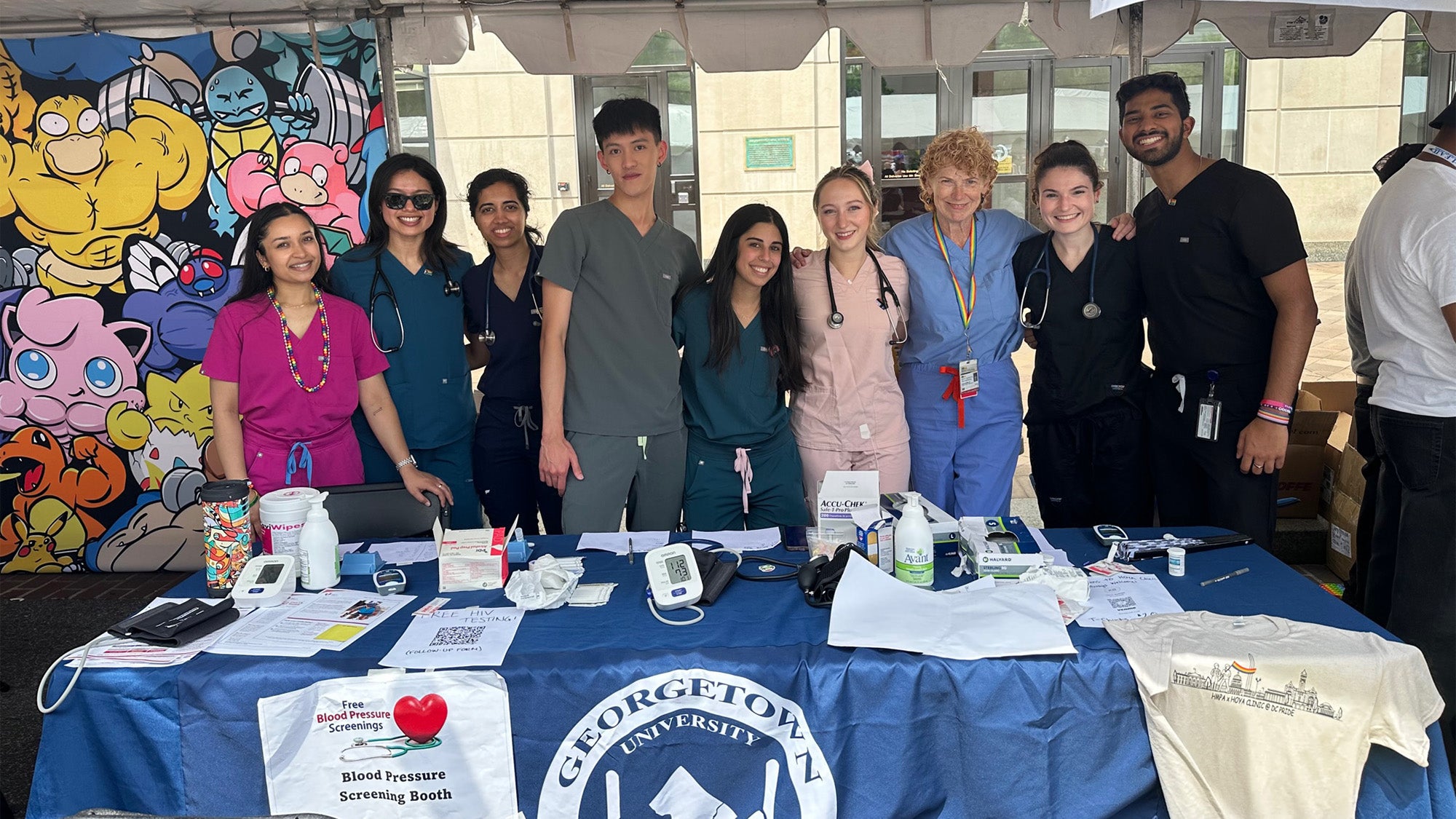 A group of volunteers wearing scrubs stand together at a table at Pride Fest 2024