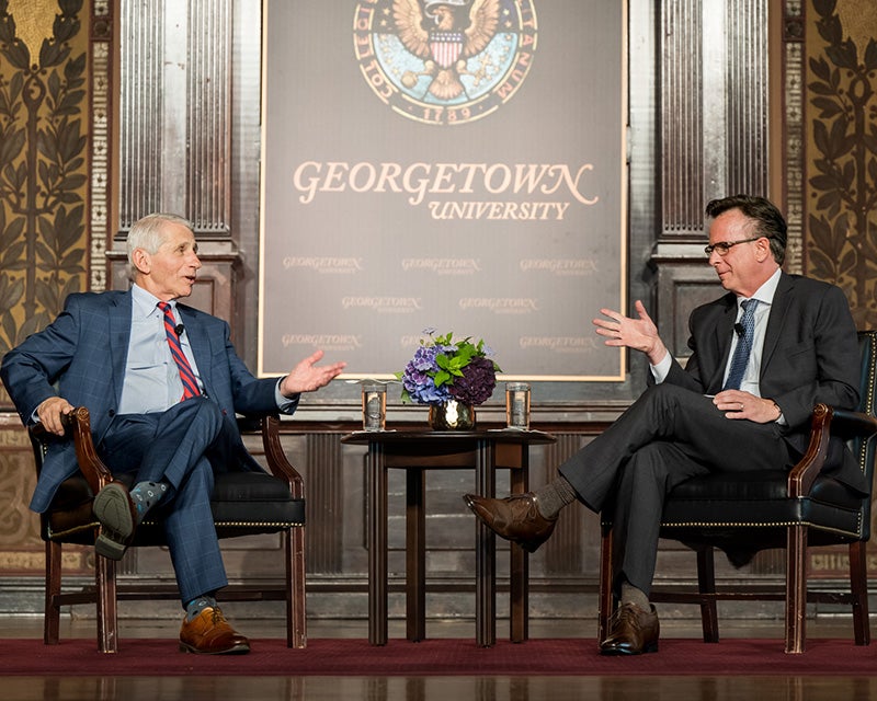 Dr. Fauci and Norman Beauchamp sit in chairs onstage in Gaston Hall