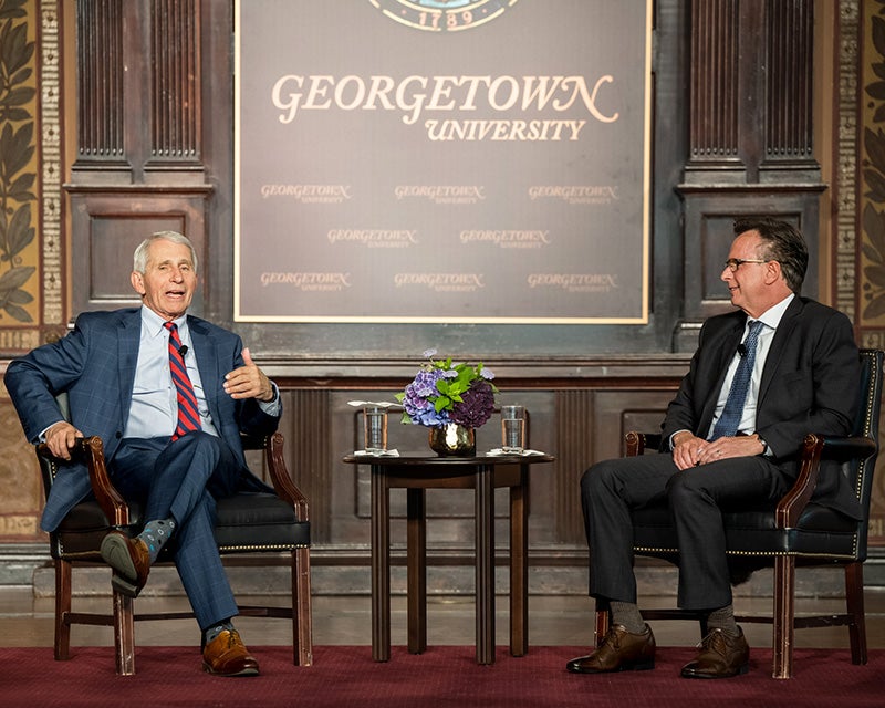 Dr. Fauci and Norman Beauchamp sit in chairs onstage in Gaston Hall