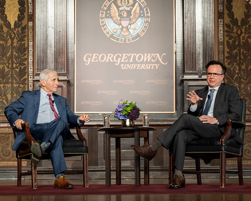 Dr. Fauci and Norman Beauchamp sit in chairs onstage in Gaston Hall