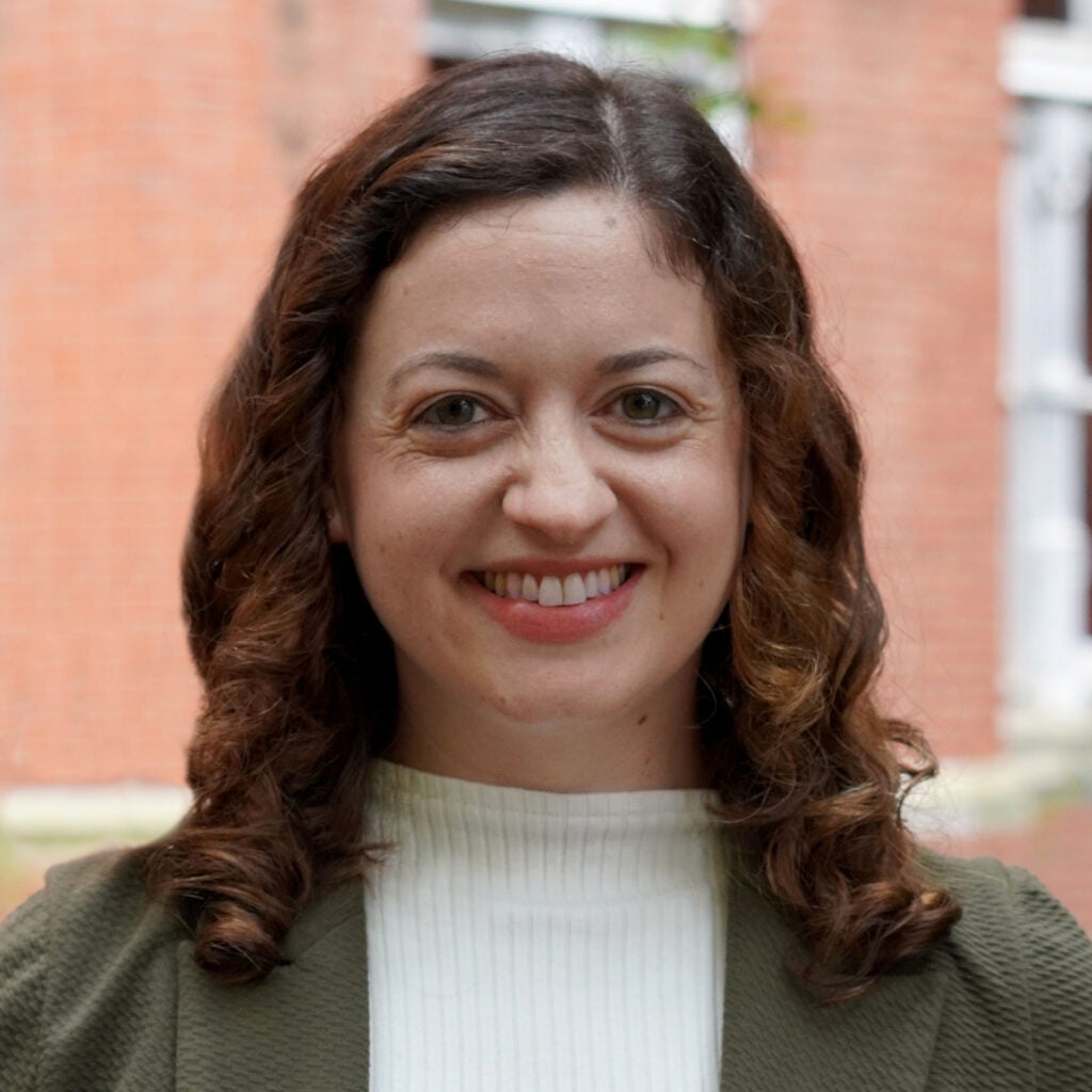 Portrait of a woman with shoulder-length, reddish brown hair wearing a white top and green jacket.