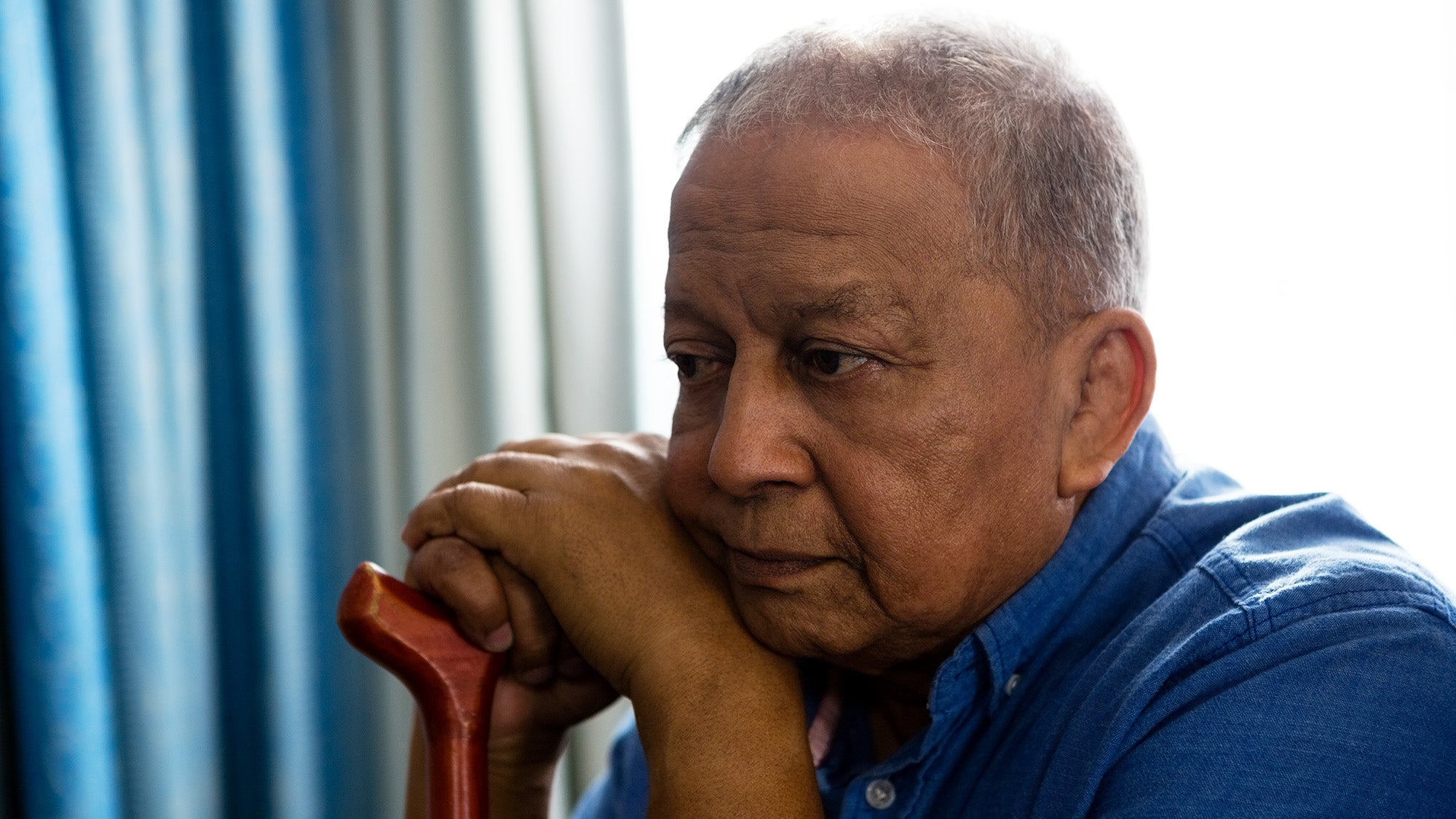 An older man looks off sadly while cradling his cane