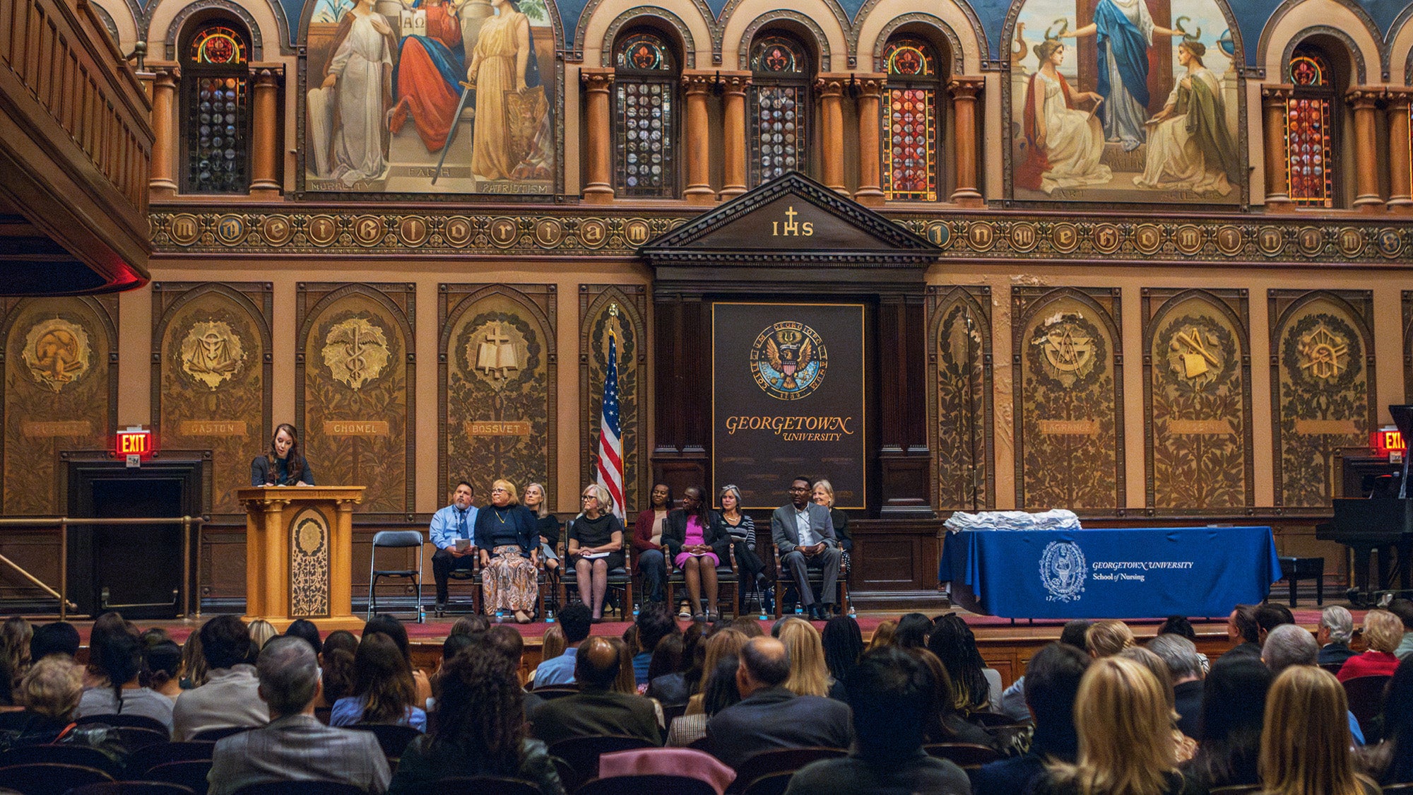 Nursing faculty and speakers line the stage in Gaston Hall before an audience