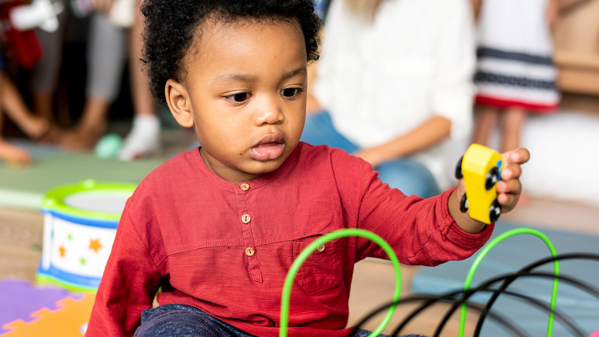 A young Black toddler plays with a toy truck on the floor