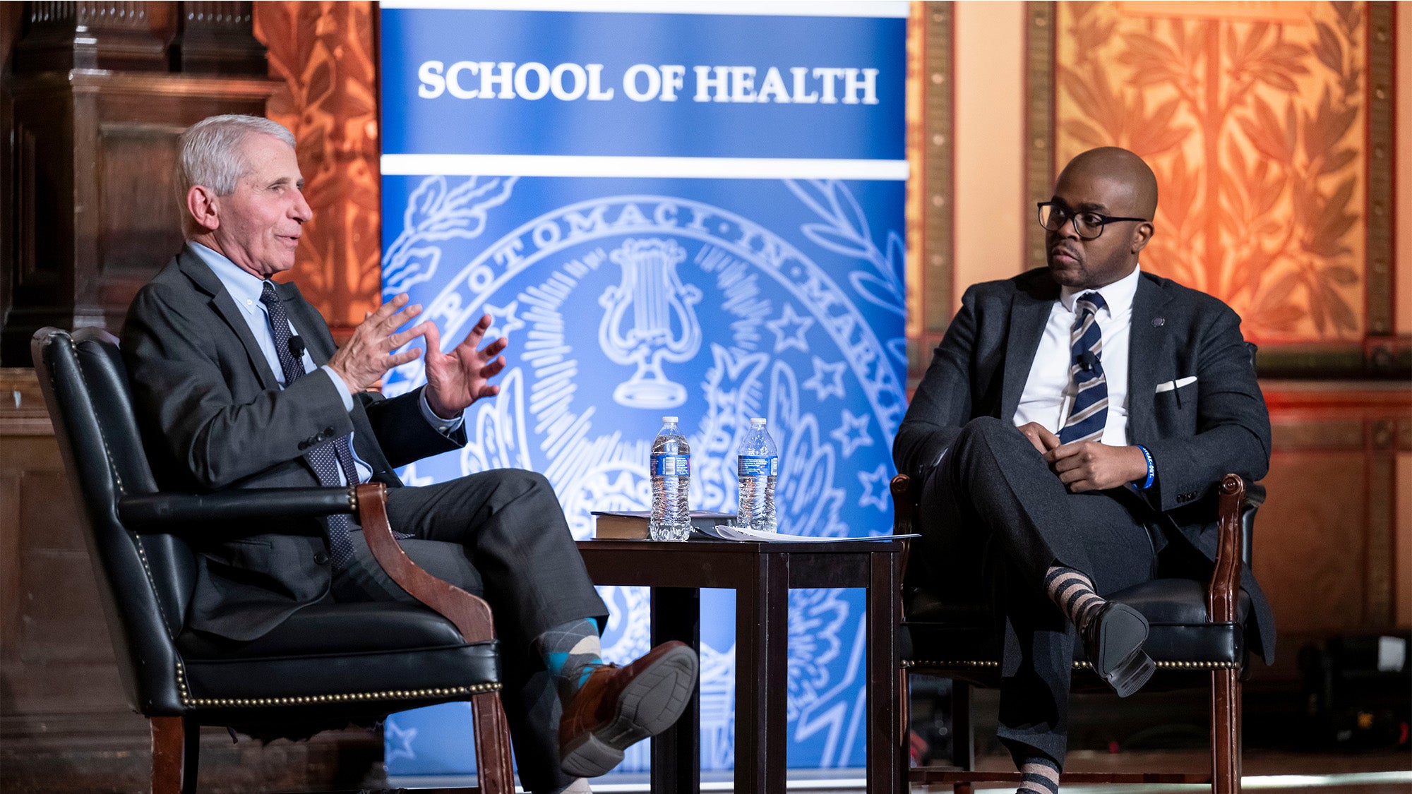 Anthony Fauci and Christopher King sit in chair on a stage in Gaston Hall