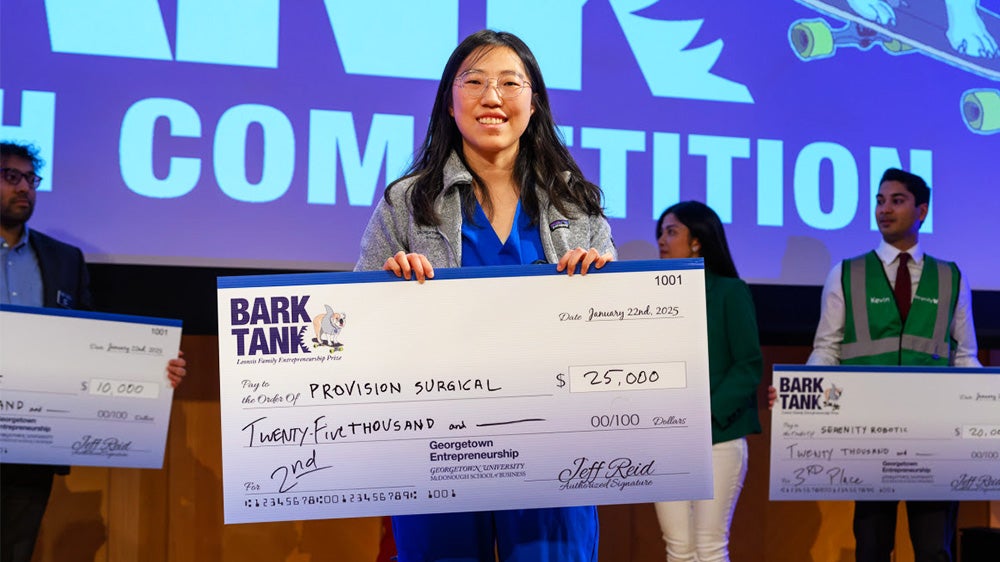 Joyce Wang holds a large cardboard check to signify her winning a prize in this year's Bark Tank pitch competition