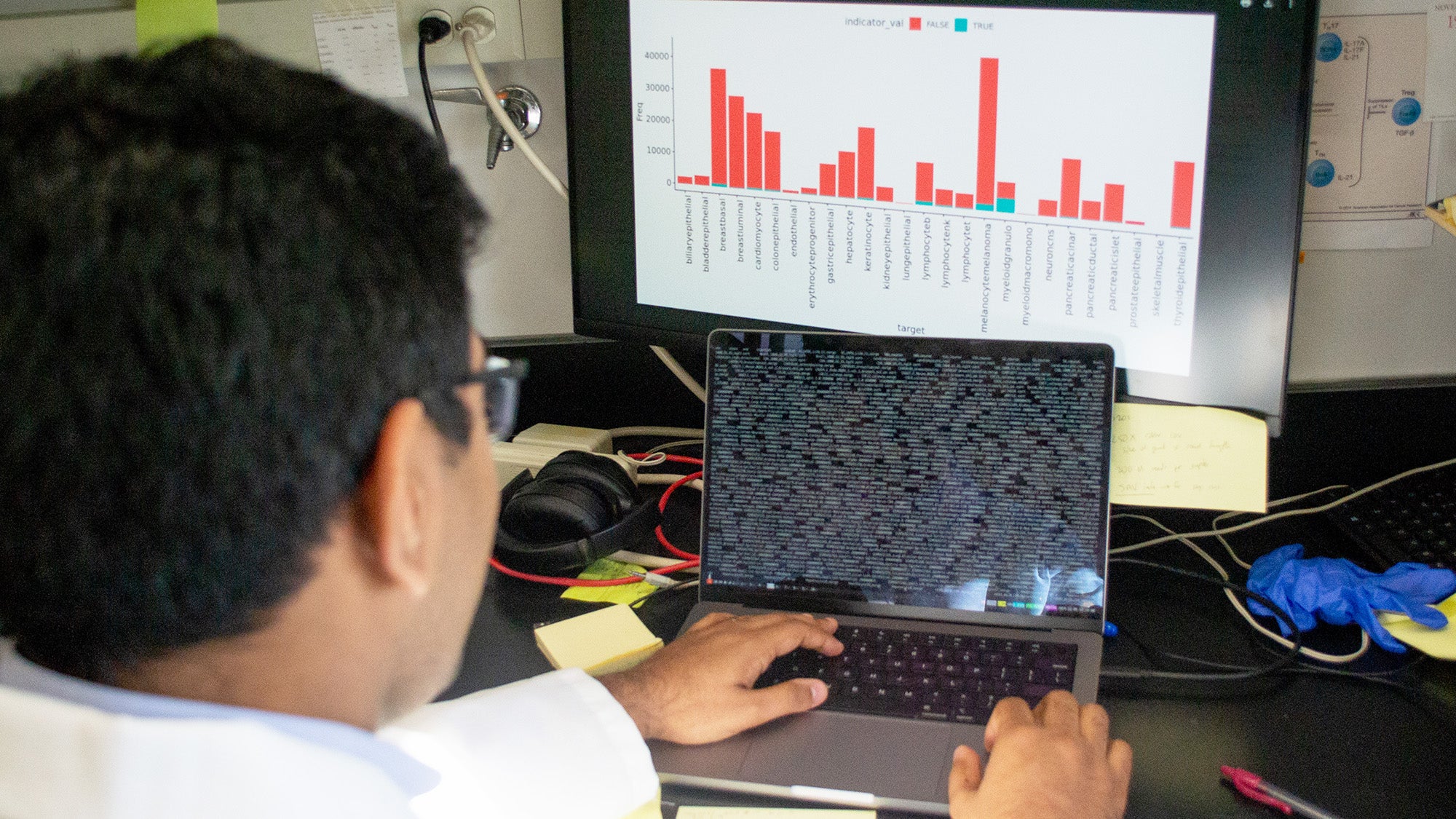 MD/PhD student Sid Jain works at a laptop with a large monitor behind it