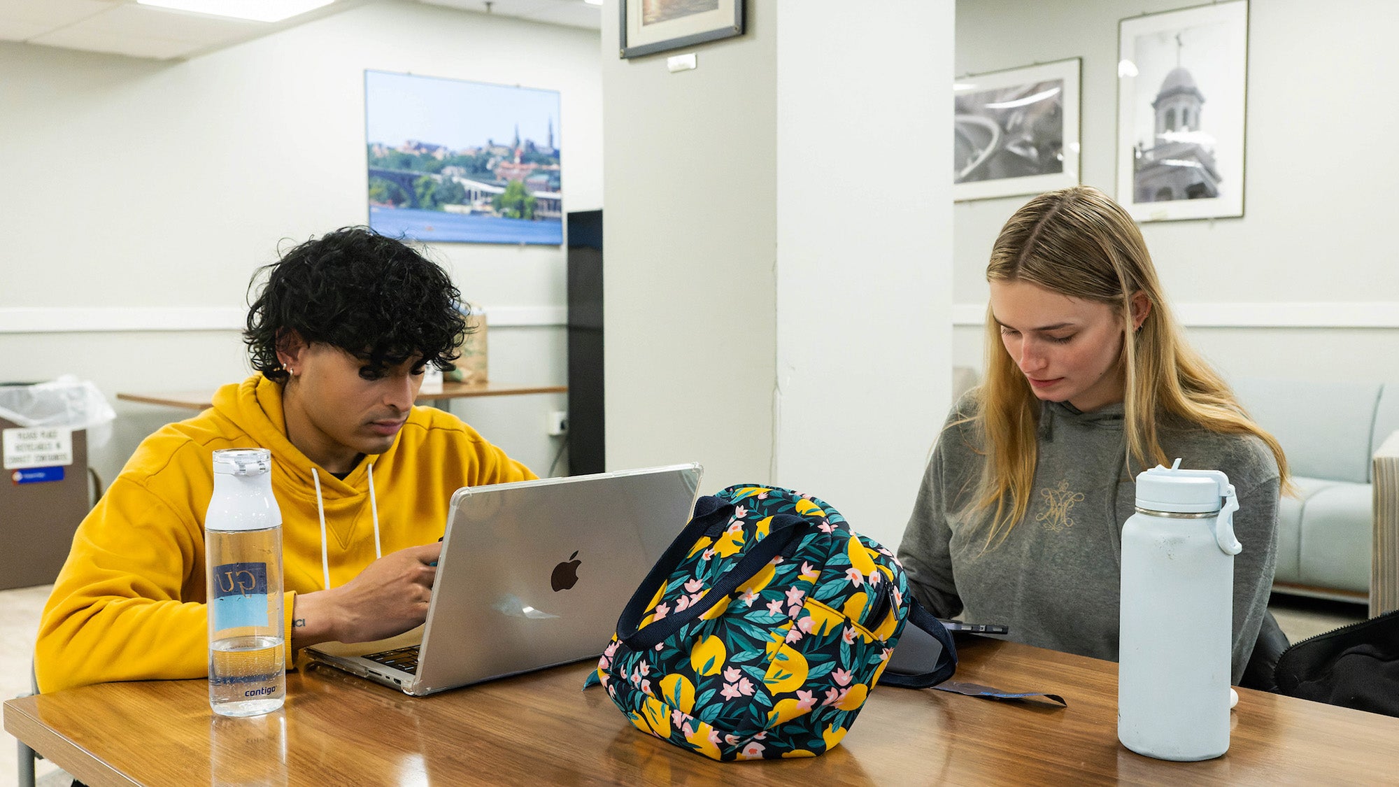 Two students use electronic devices at a table in the library