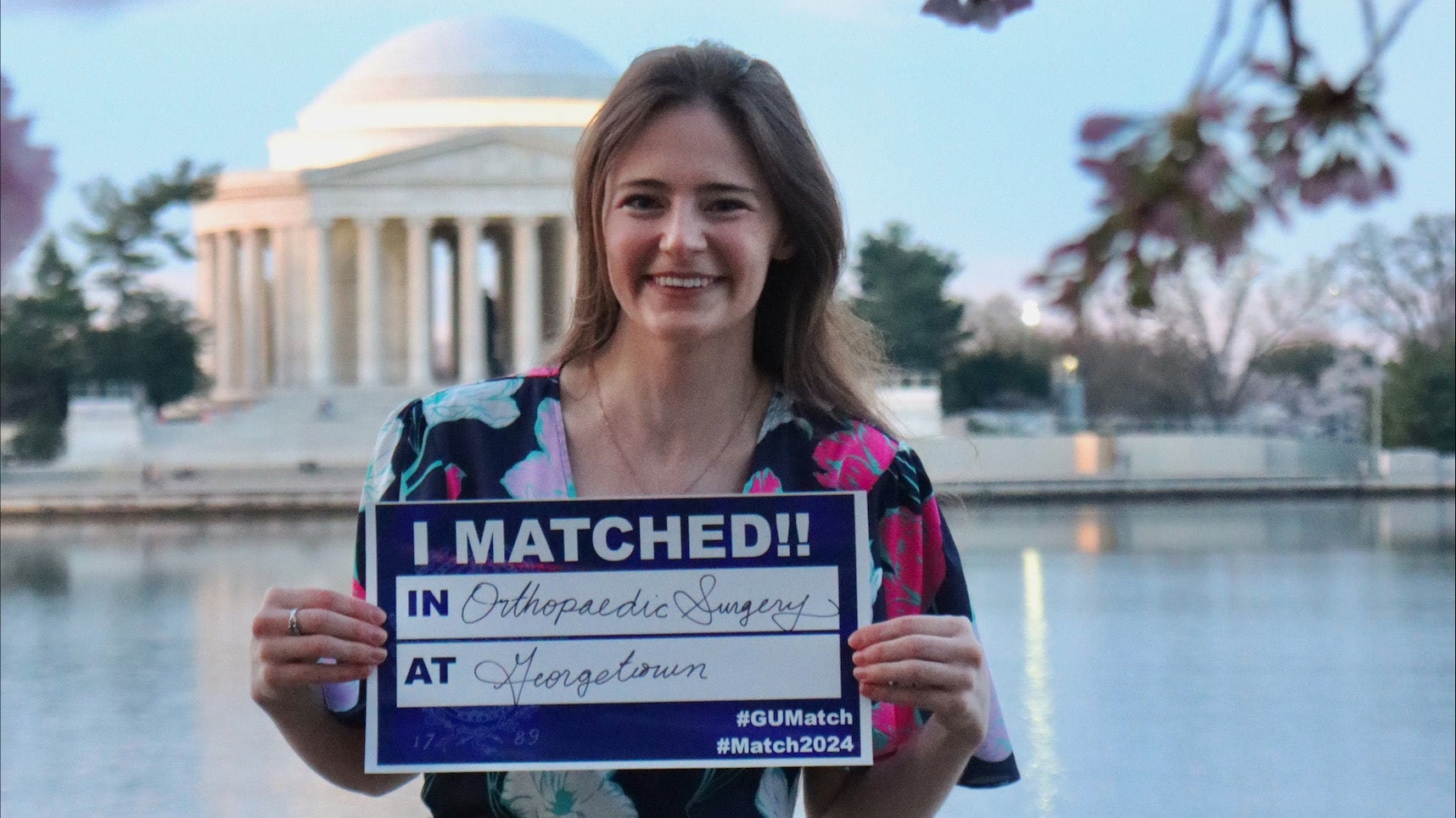 Sarah Lucas holds a sign that reads I Matches in Orthopaedic Surgery at Georgetown; in the background are cherry blossoms and the Jefferson Memorial