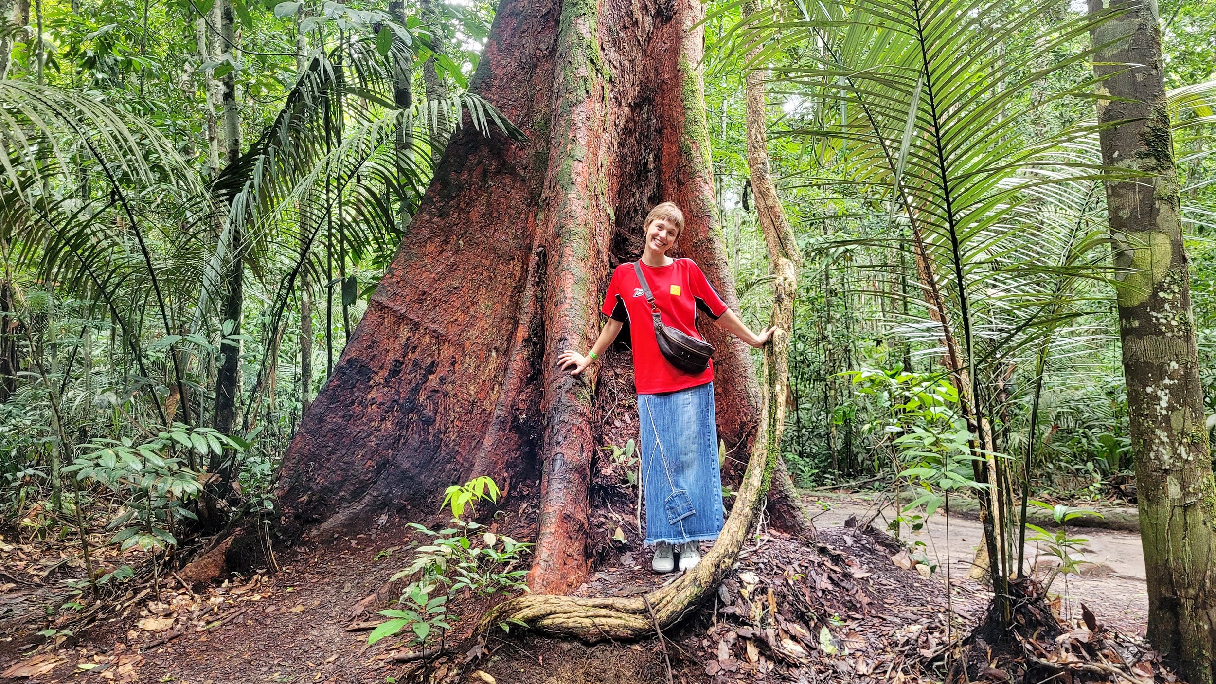 Lexie Meger stands before a large tree in the Brazilian rainforest