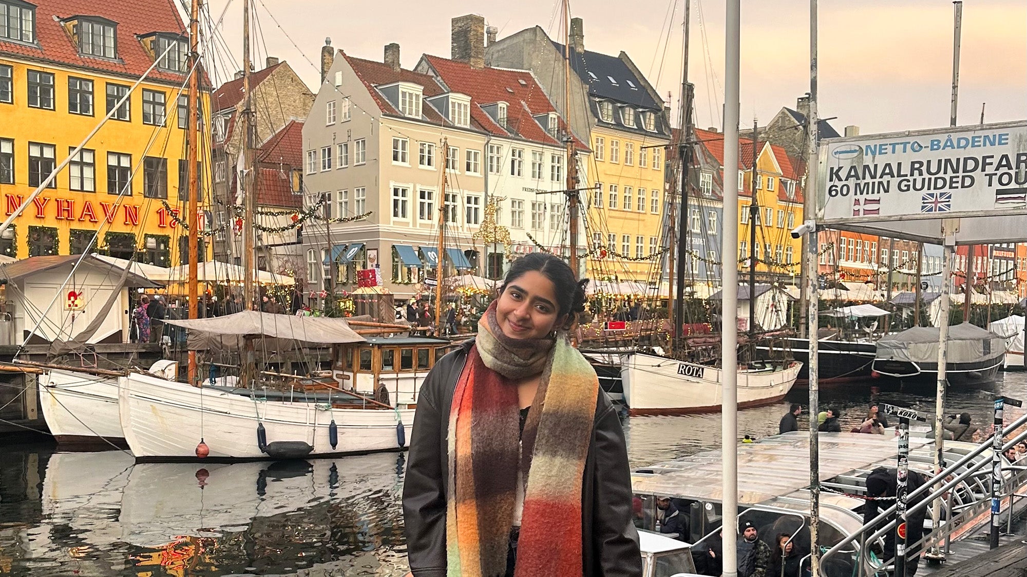 Dhruvi Parikh stands on the shore of the Copenhagen harbor with rows of colorful houses behind her