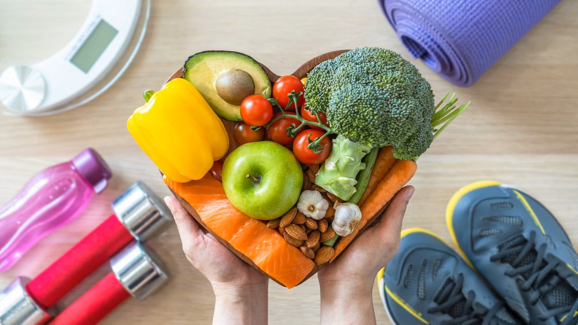 Fruits and veggies in a heart shaped bowl on a table with exercise equipment in the background