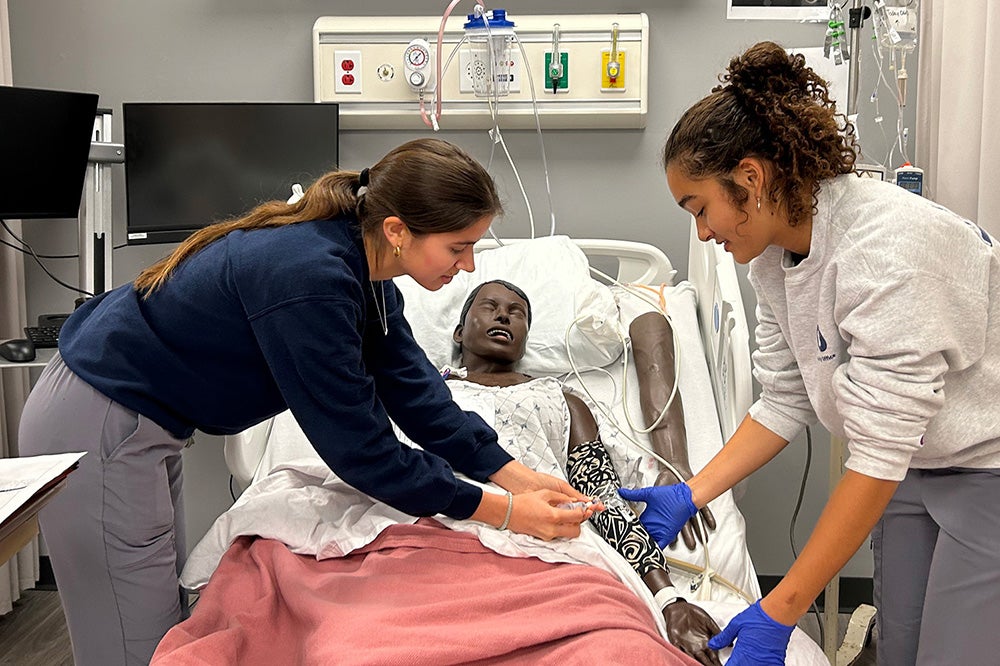 Two nursing students tend to a SIM Lab dummy