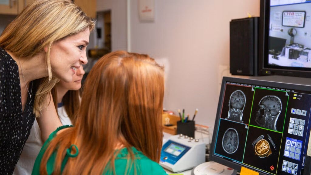 A professor looks on as students work at a computer with brain scans on the display