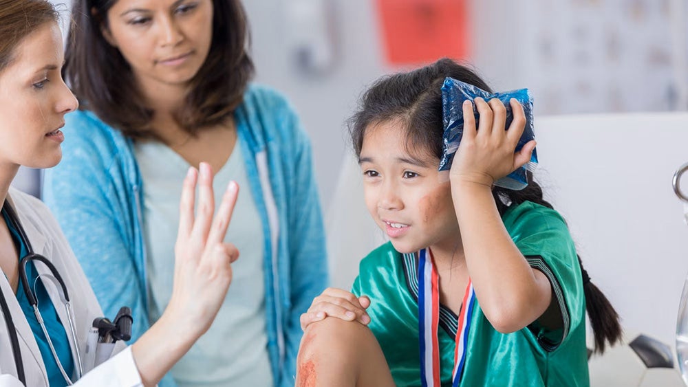 Medical professionals care for a female child athlete holding an ice pack to her head