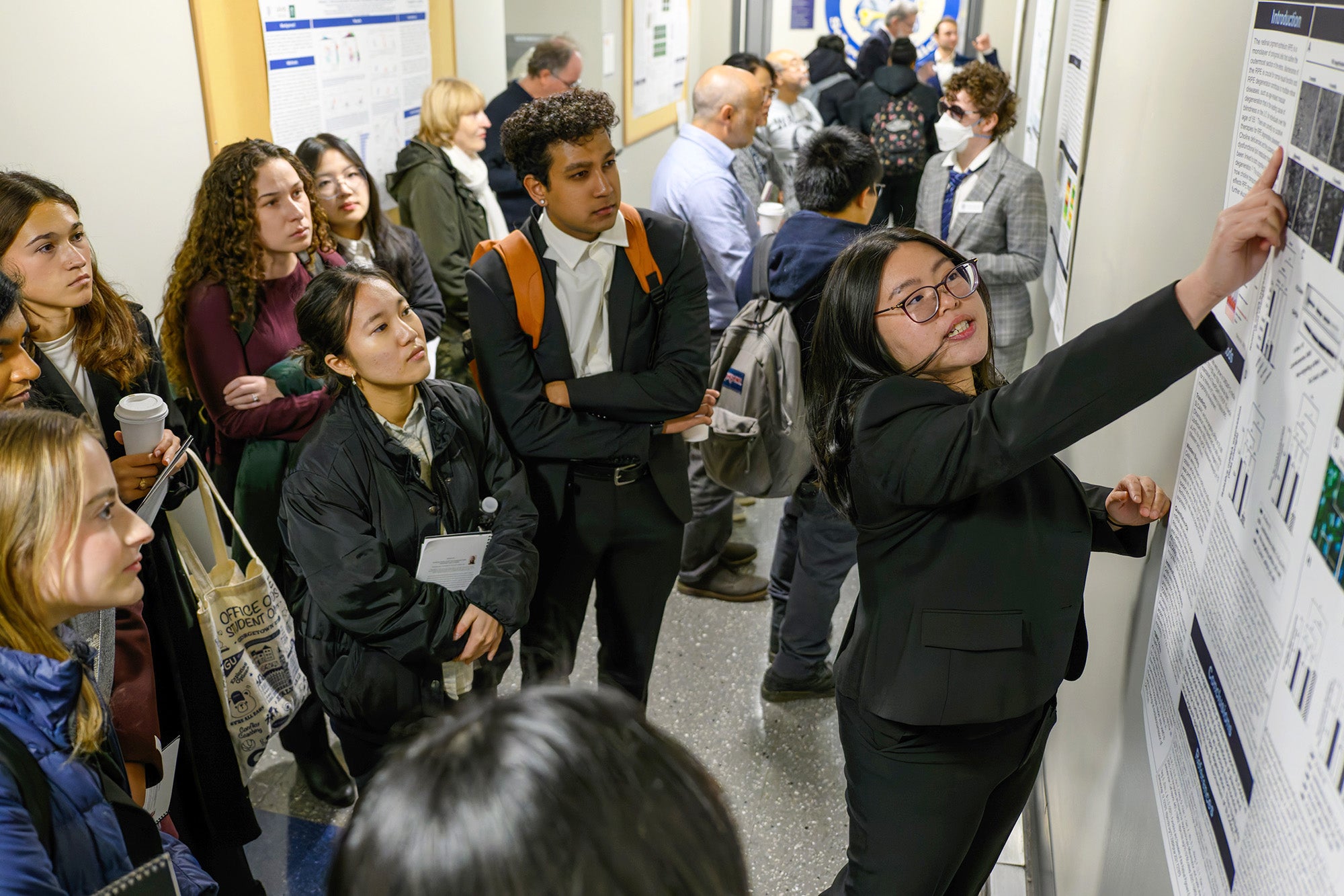 A student in the M.S. in Biochemistry program presents her research poster to other students standing in a hallway