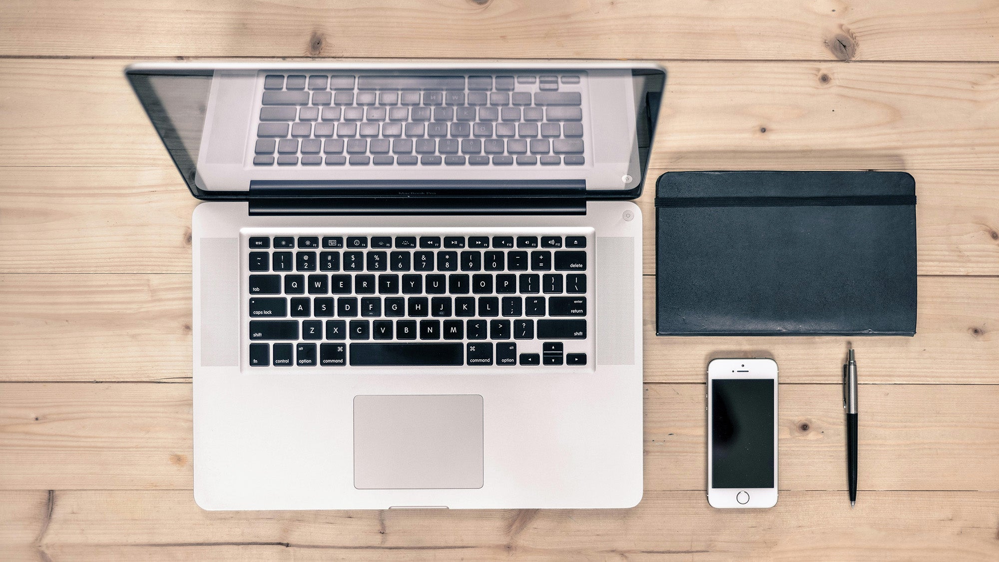 A laptop, phone, notebook and pen on a tabletop