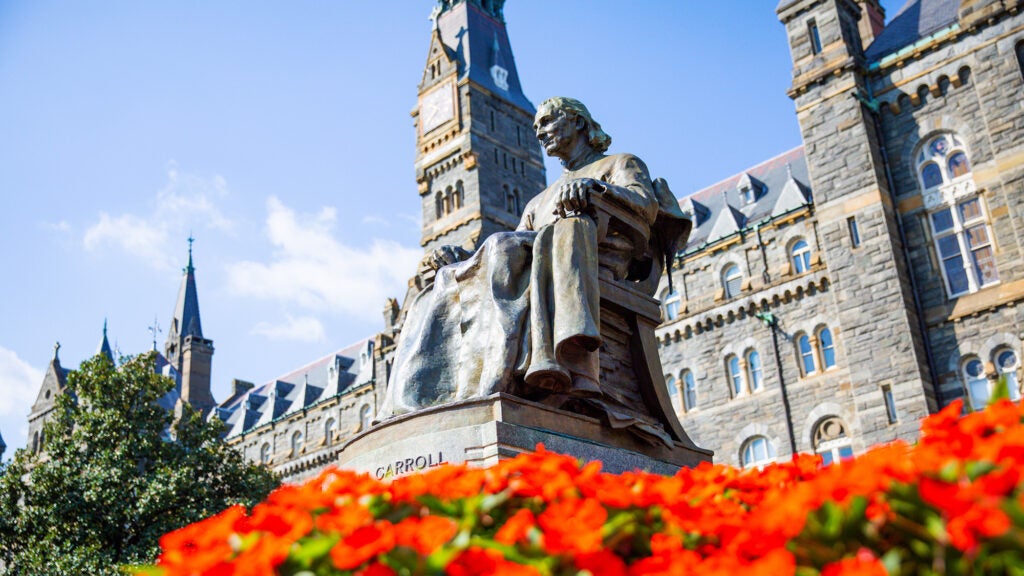 John Carroll statue on a sunny day with flowers in bloom and Healy Hall in the background