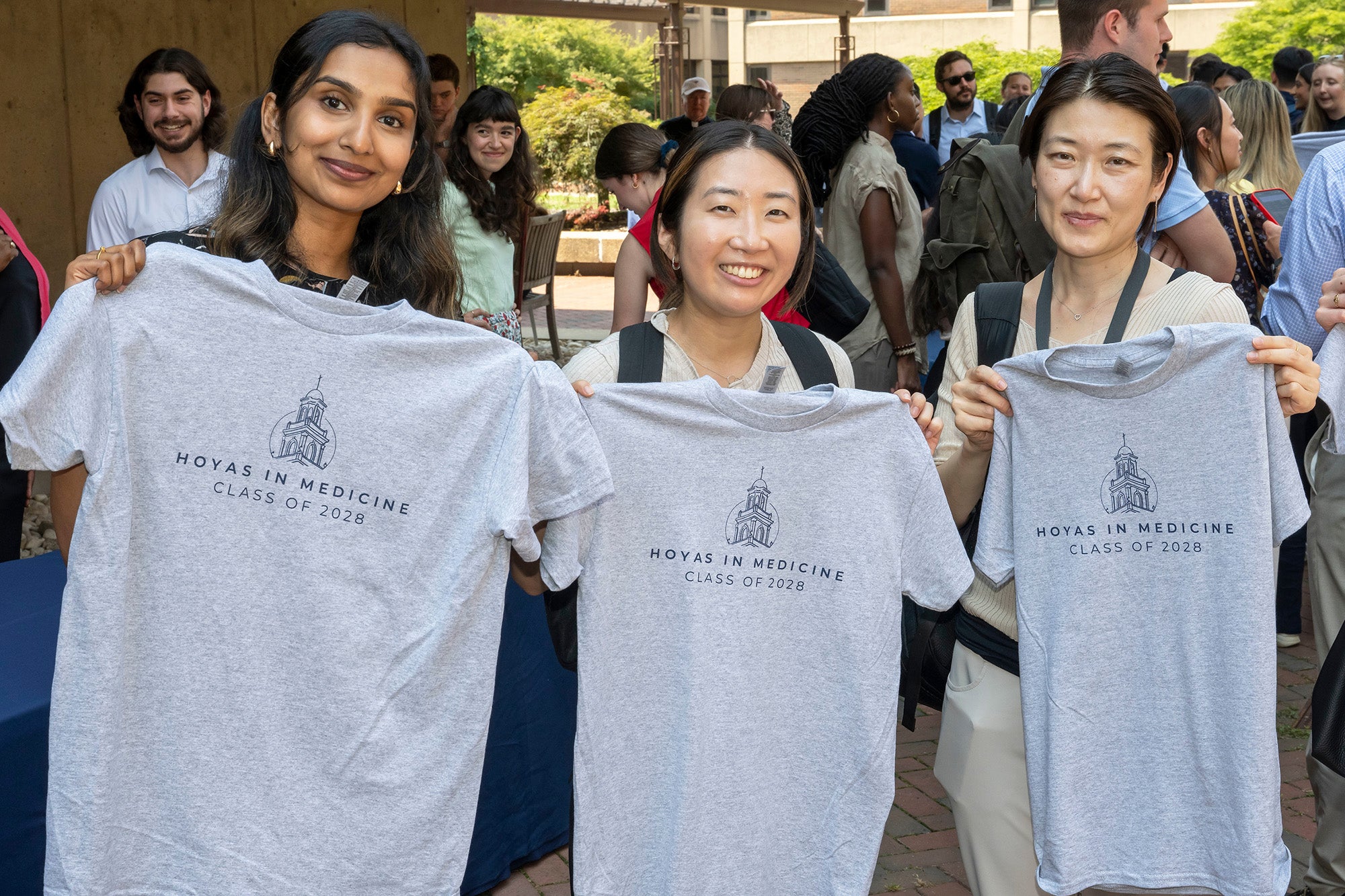 Three medical students stand together holding t-shirts