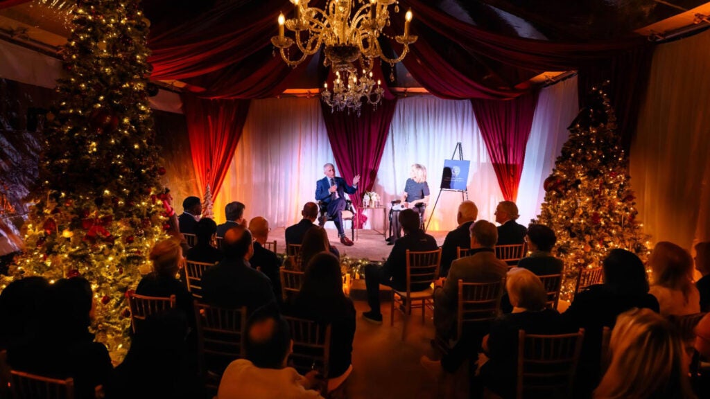 Fauci and a woman sit in chairs before an audience amid Christmas decorations