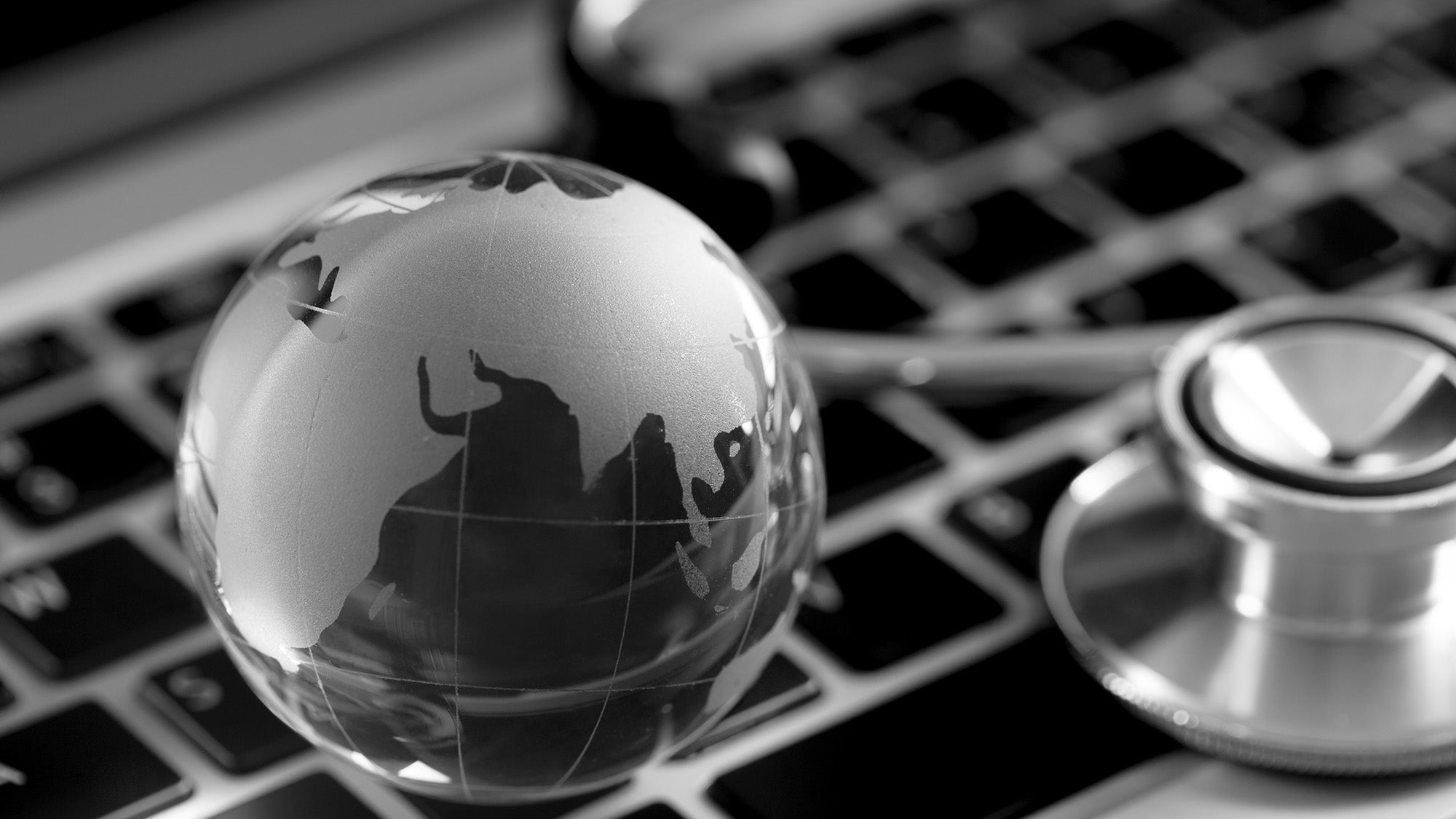 Photo illustration of a clear globe model on a computer keyboard next to a stethoscope