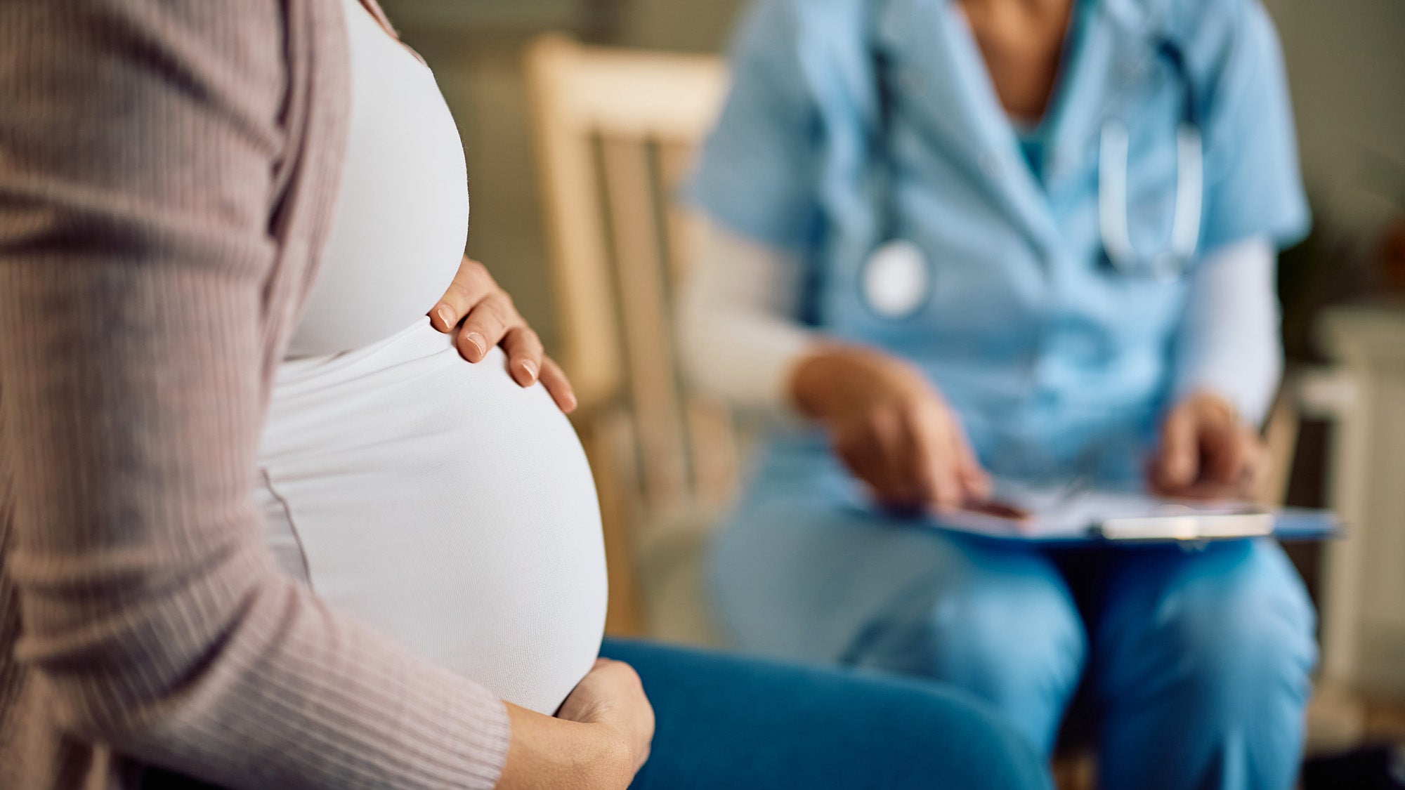 A pregnant person sits adjacent to a health care professional in medical uniform