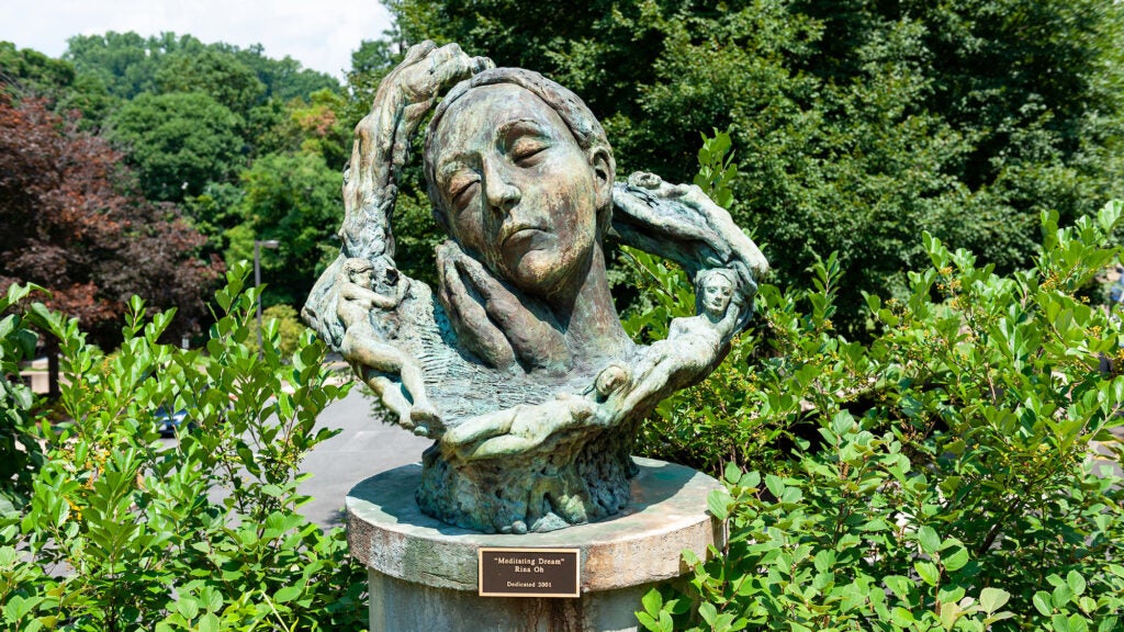A sculpture of a woman's face sits on a pedestal amid green plants