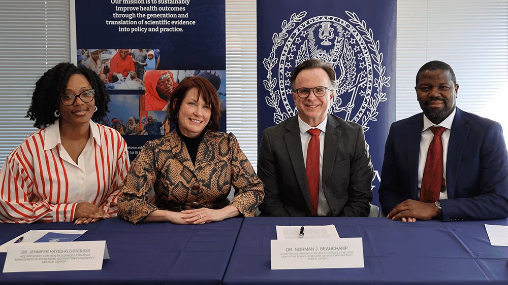 Four individuals sit at a table to sign an agreement