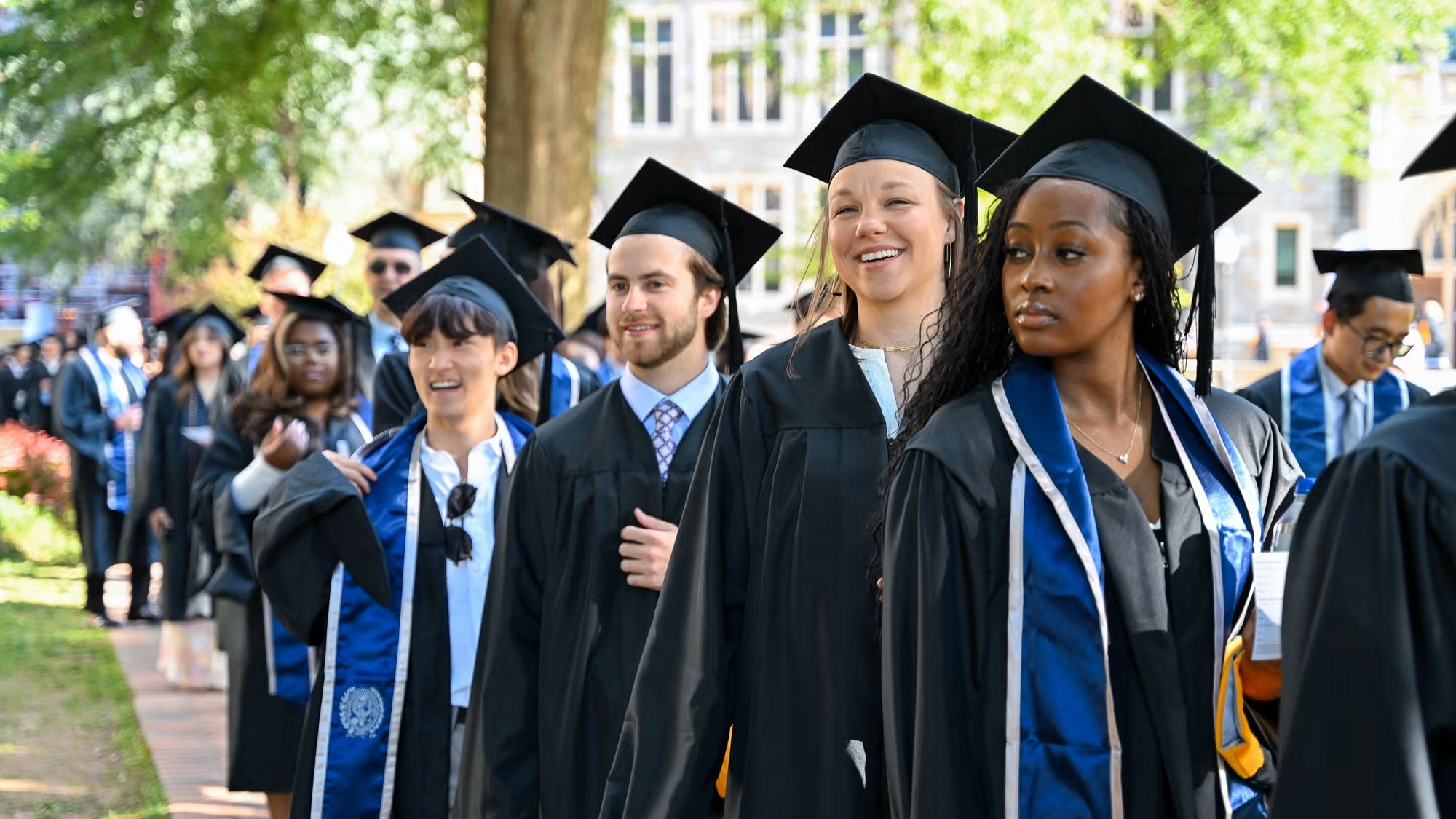 Master's students in academic regalia process across campus