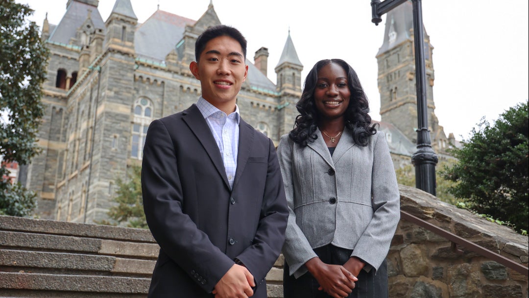 Two individuals stand on the steps outside Healy Hall