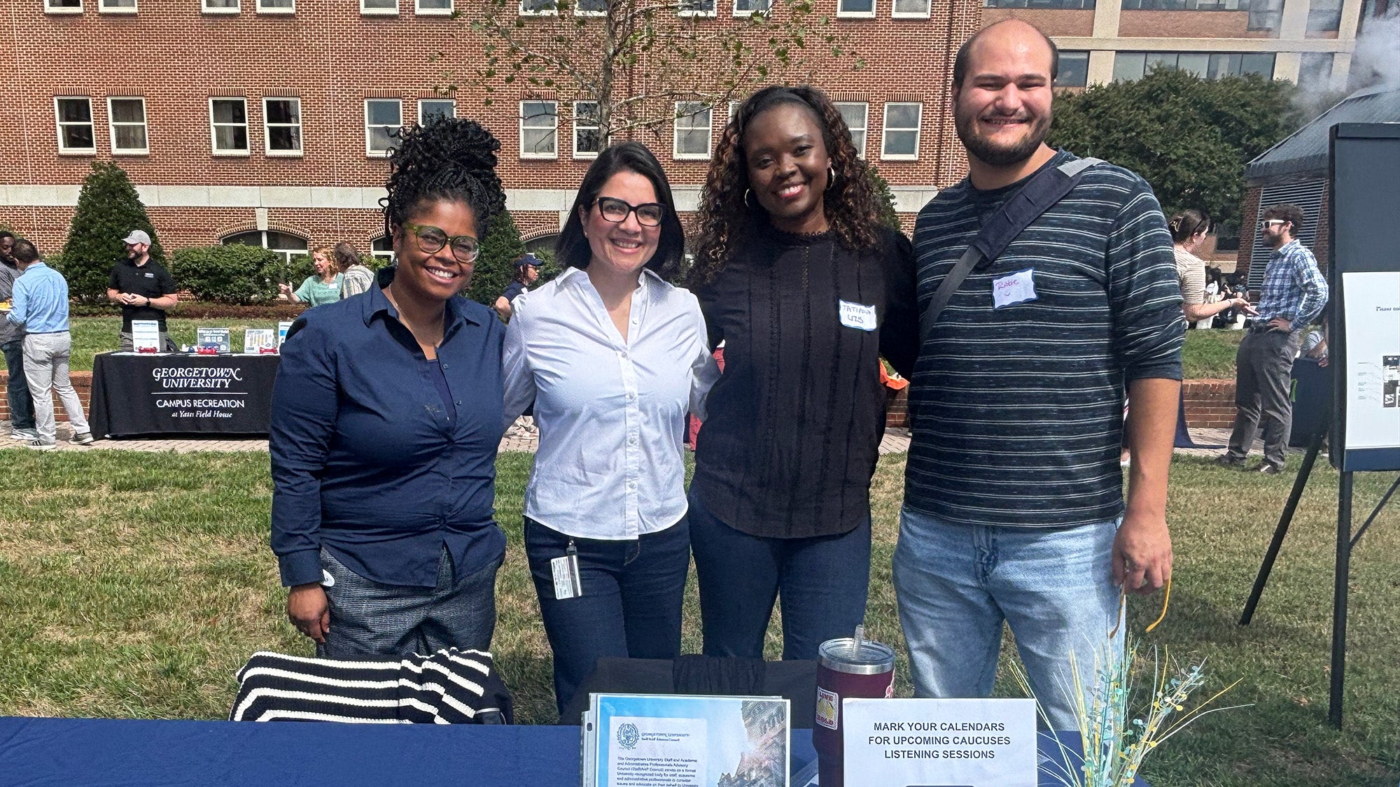 Four individual stand behind a table at an outdoor event