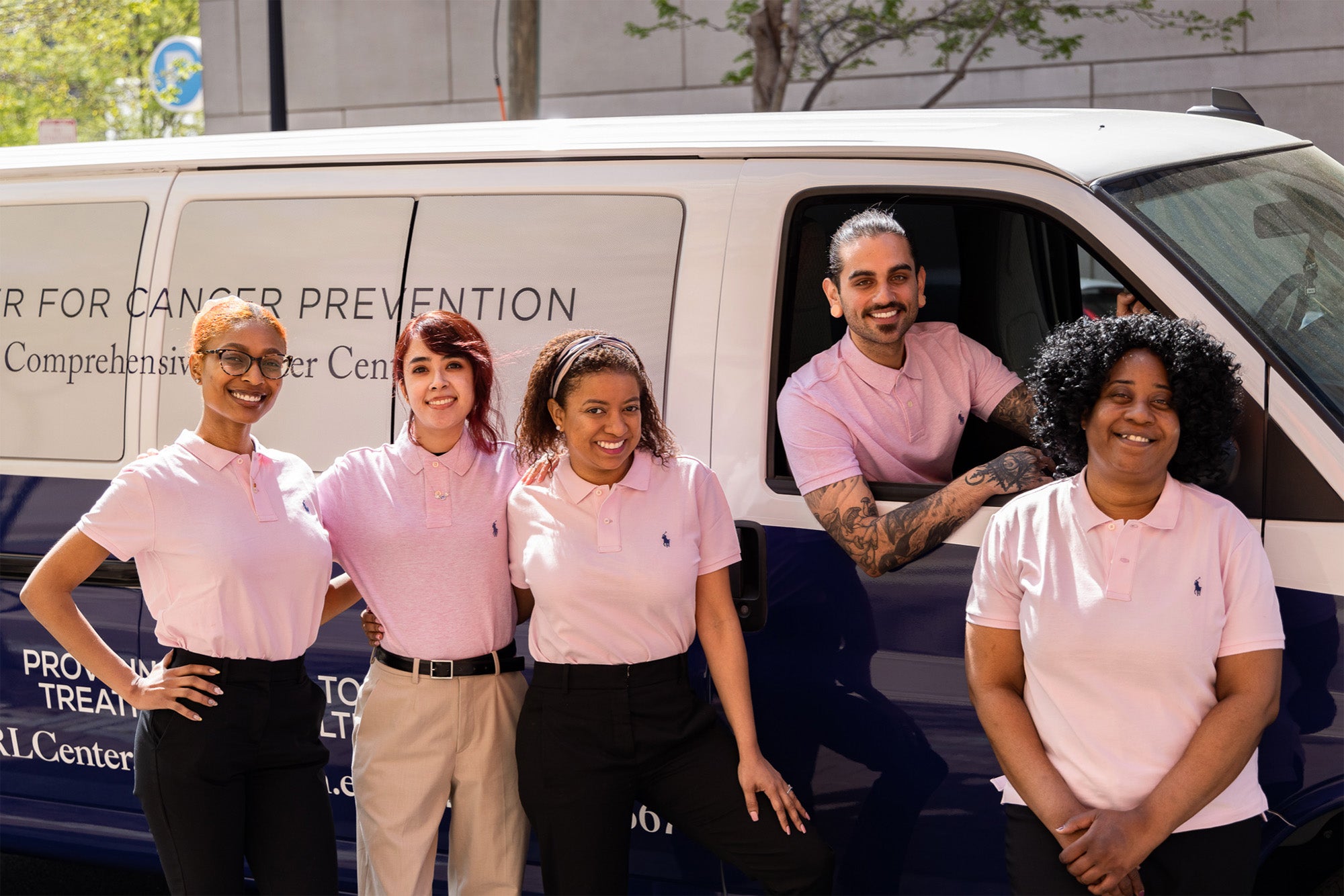Five members of the Ralph Lauren Center staff sit and stand next to the van used to transport patients to and from screenings for cancer