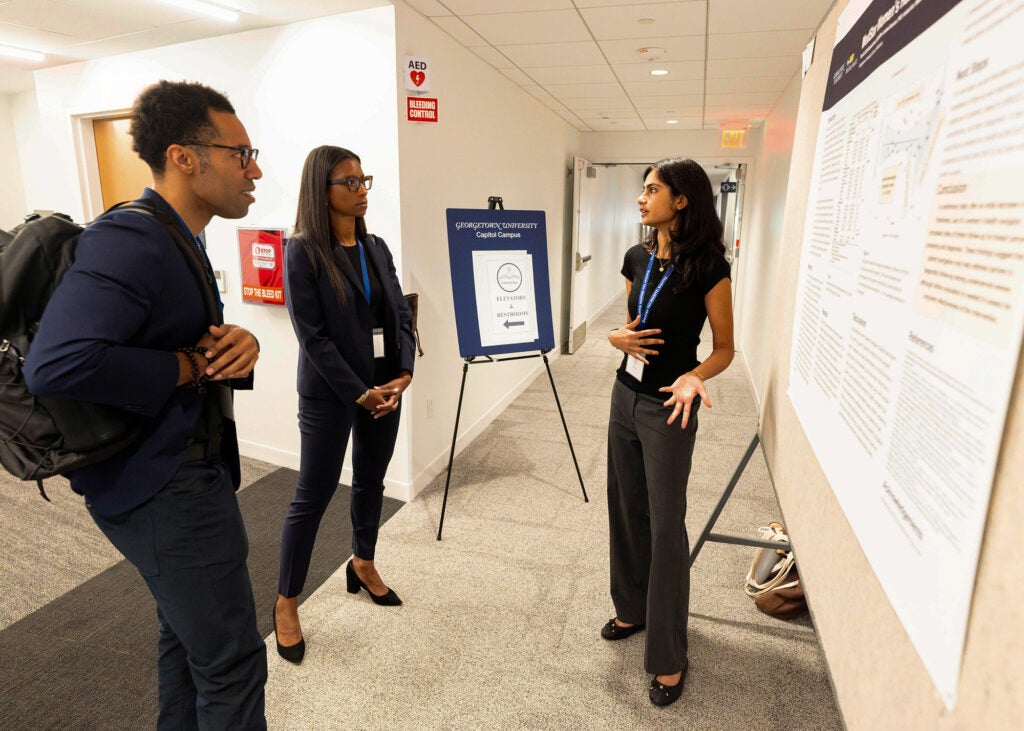 A young woman presents her poster to two conference attendees