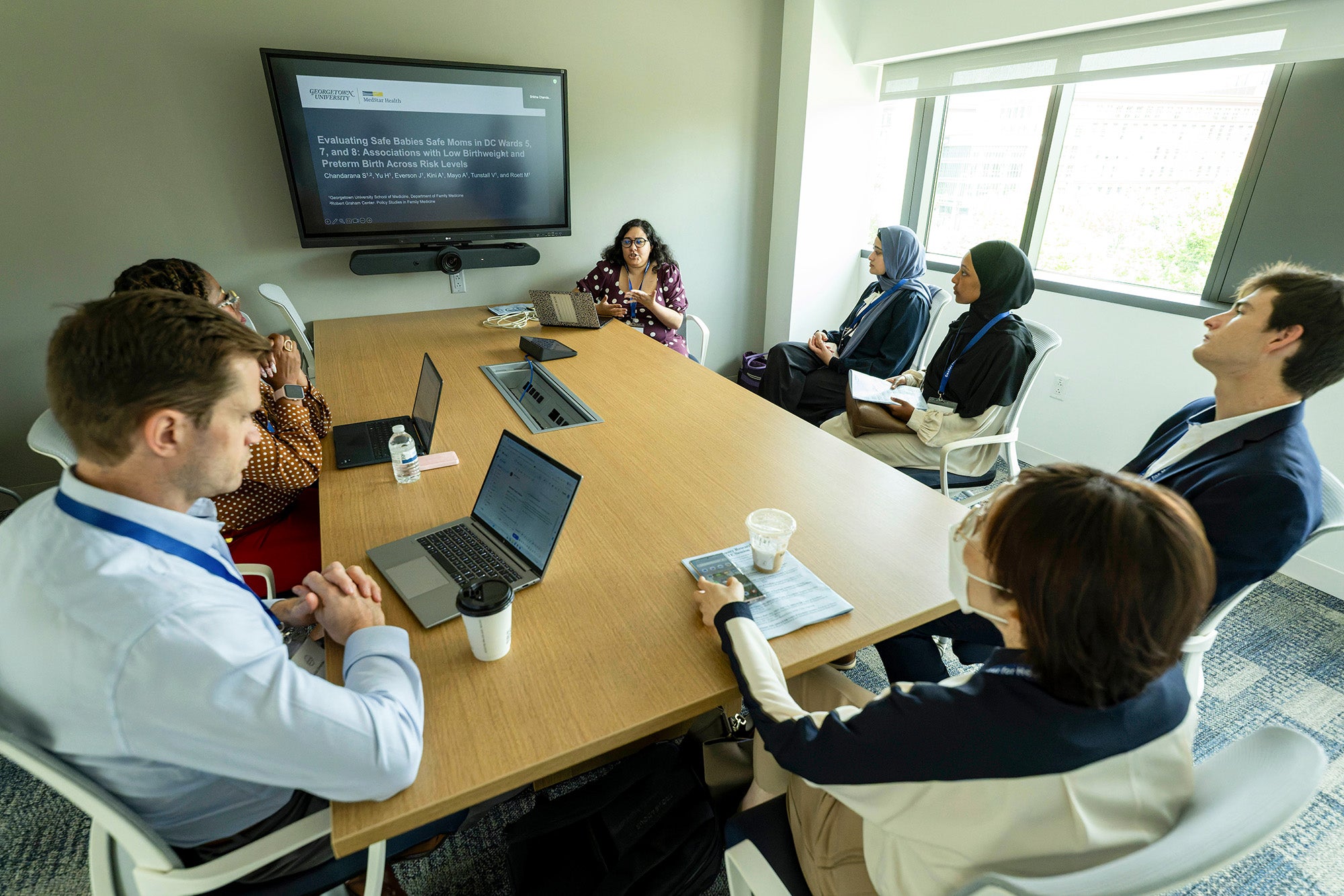 Several individuals are seated around a table in a classroom
