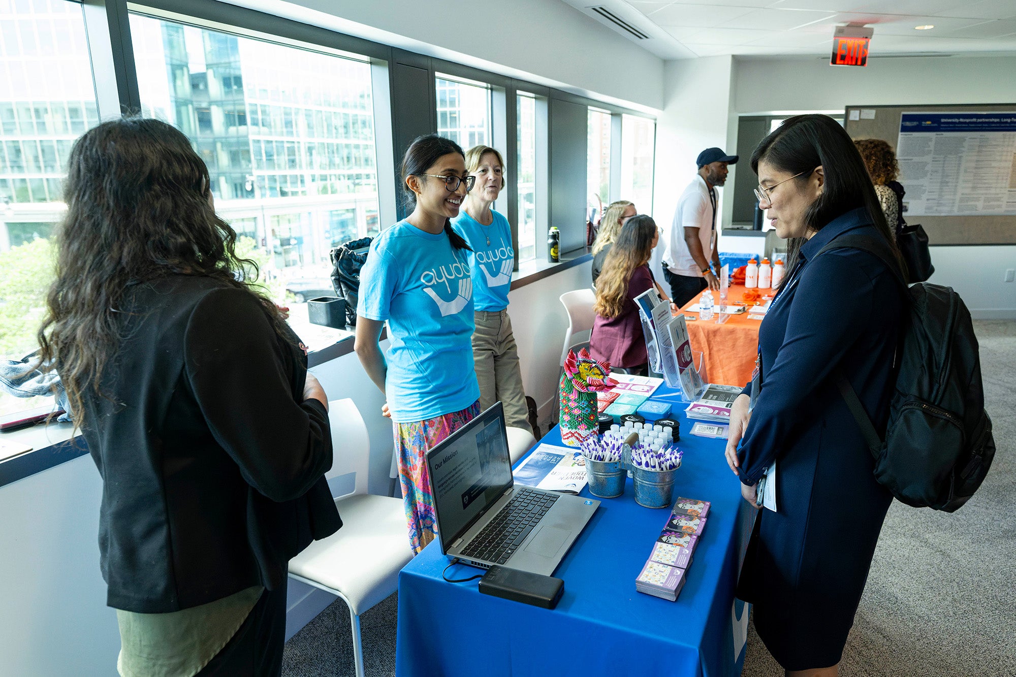 A woman stands behind a table speaking with conference attendees